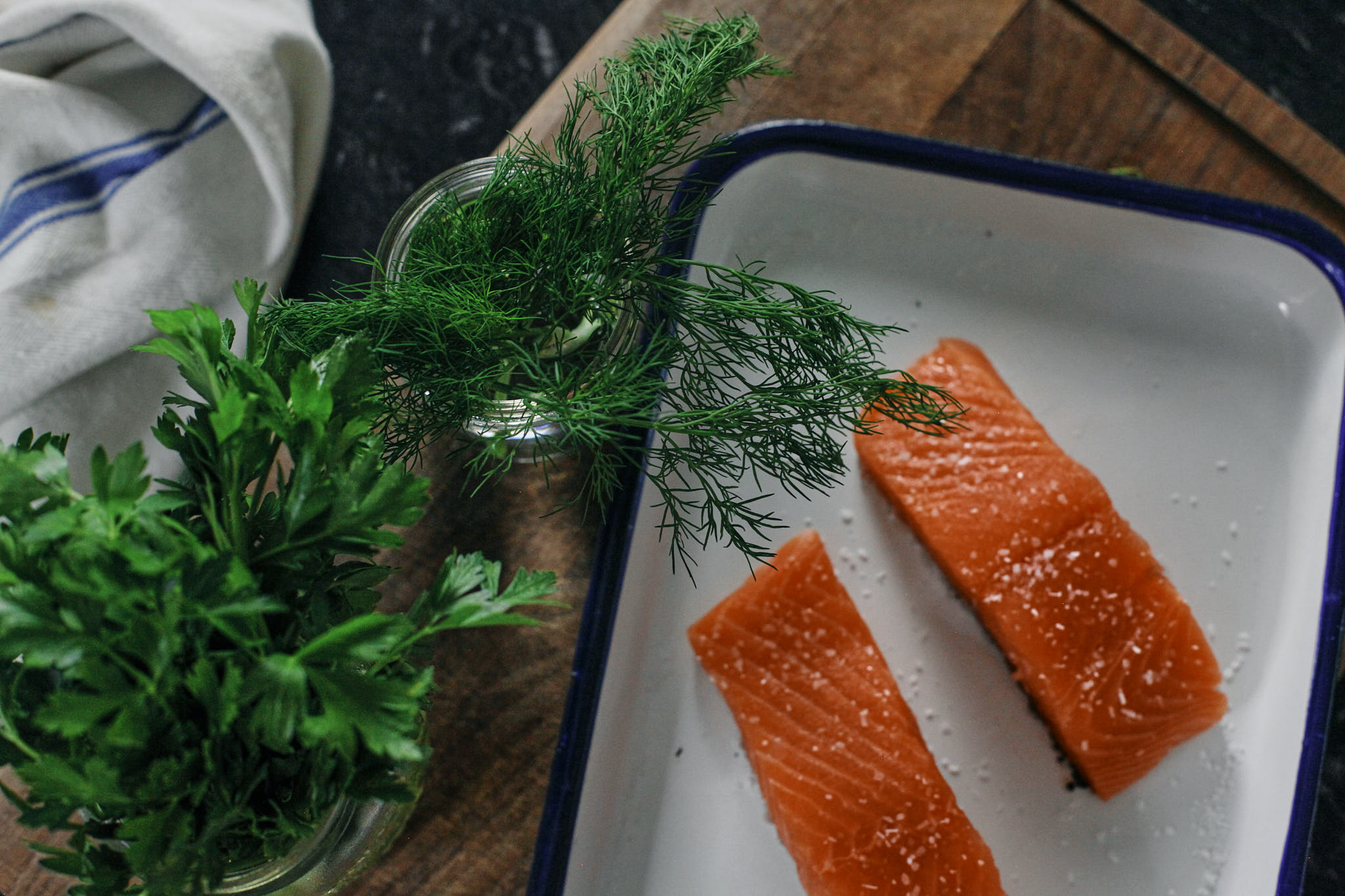 raw salmon filets next to green herbs
