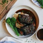 red wine braised short ribs over mashed potatoes and broccolini with a red wine sauce poured over top