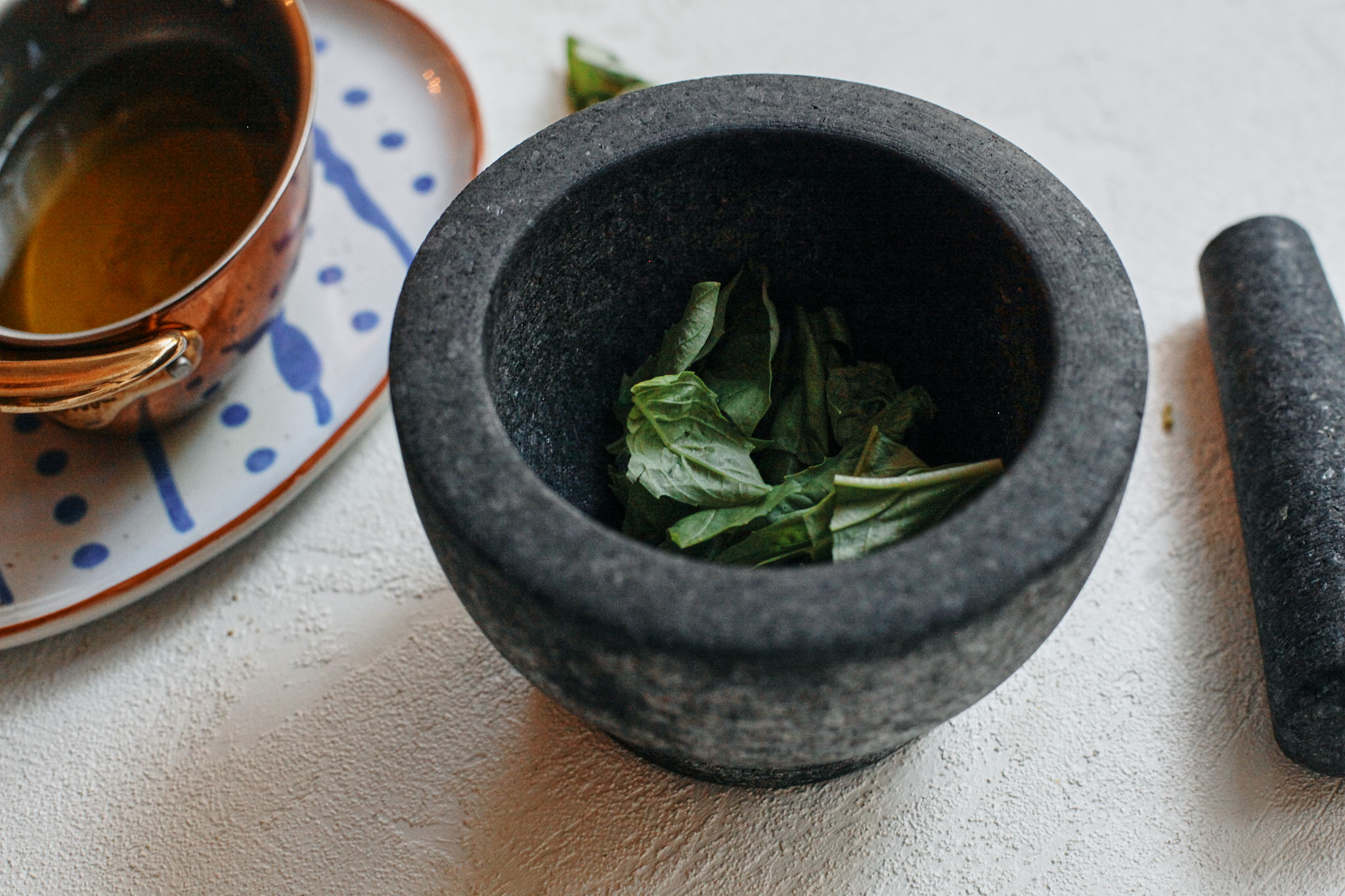 basil in a mortar and pestle about to be made into a basil oil