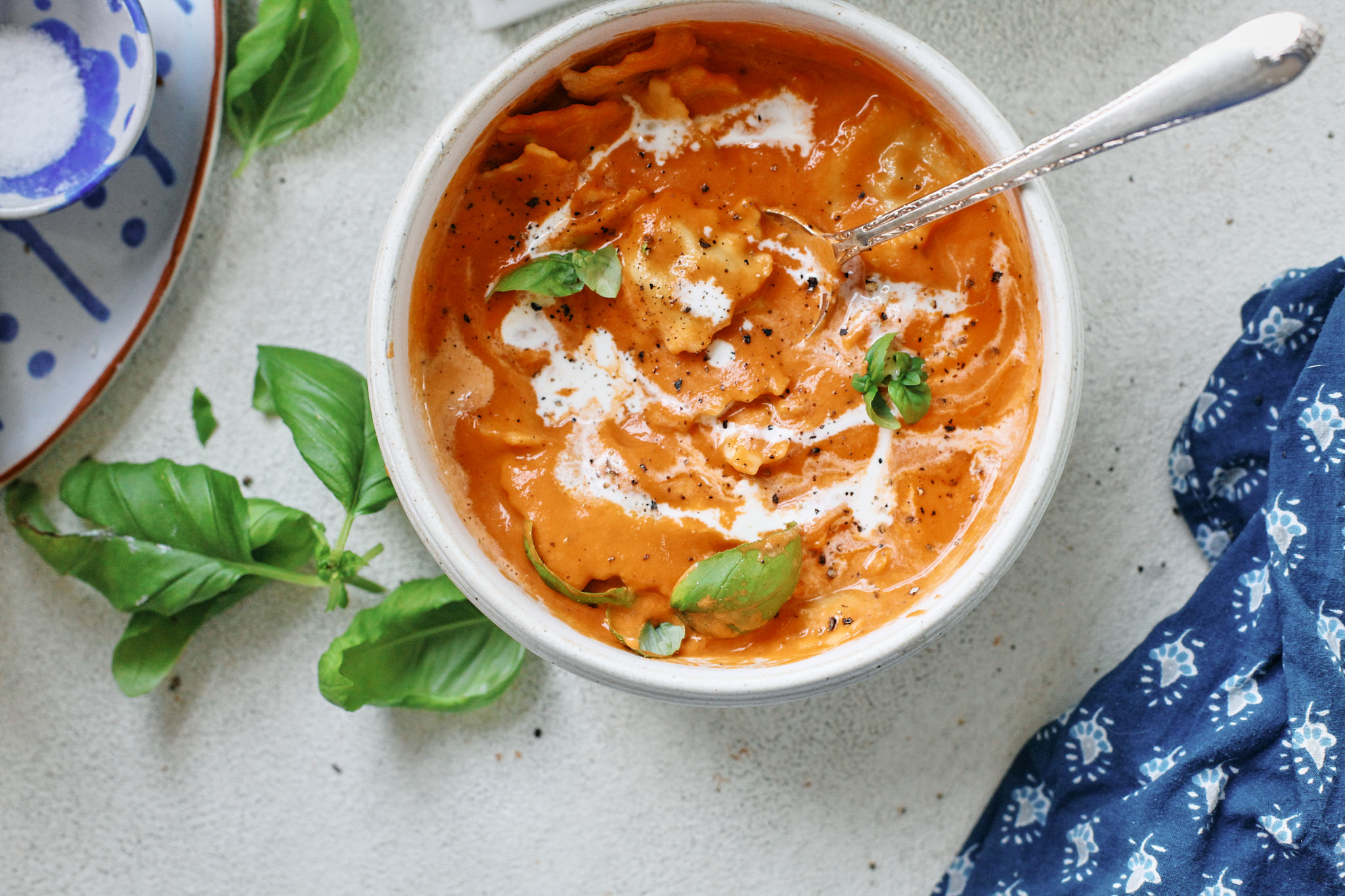 Creamy Tomato Ravioli Soup in a white bowl with basil garnish and a drizzle of cream, perfect cozy dinner recipe