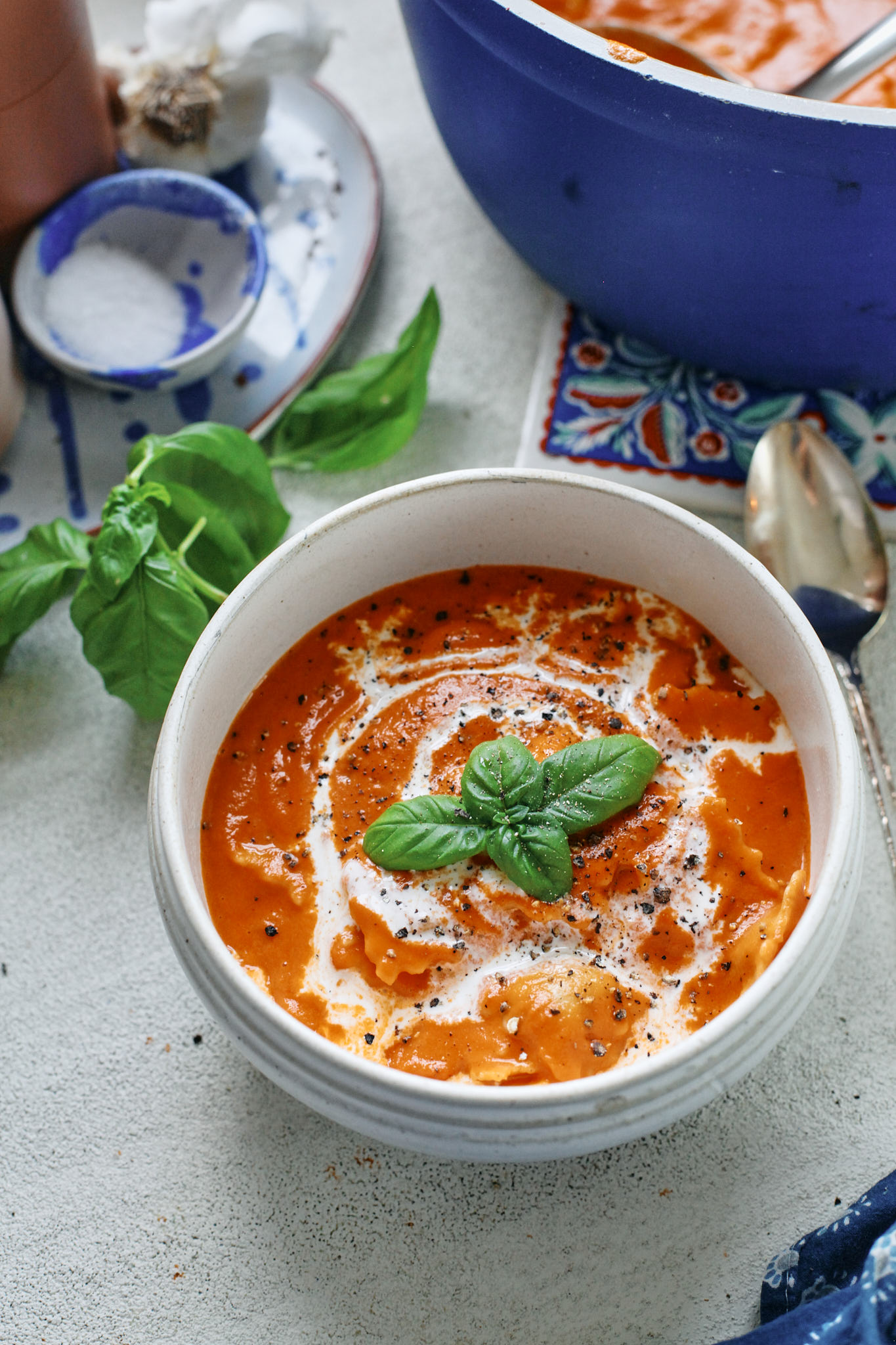 Creamy Tomato Ravioli Soup in a white bowl with basil garnish and a drizzle of cream, perfect cozy dinner recipe