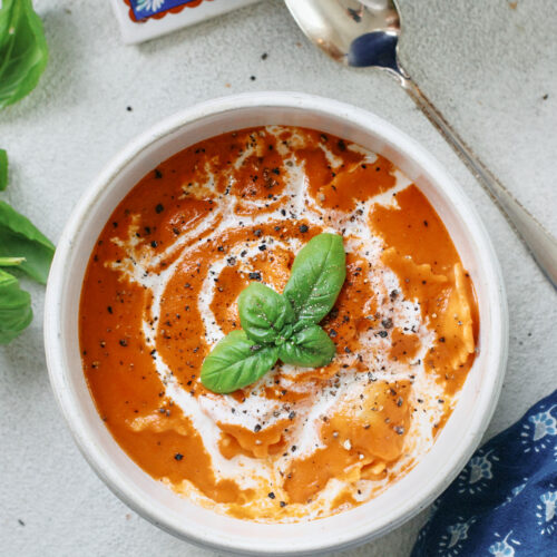 Creamy Tomato Ravioli Soup in a white bowl with basil garnish and a drizzle of cream, perfect cozy dinner recipe