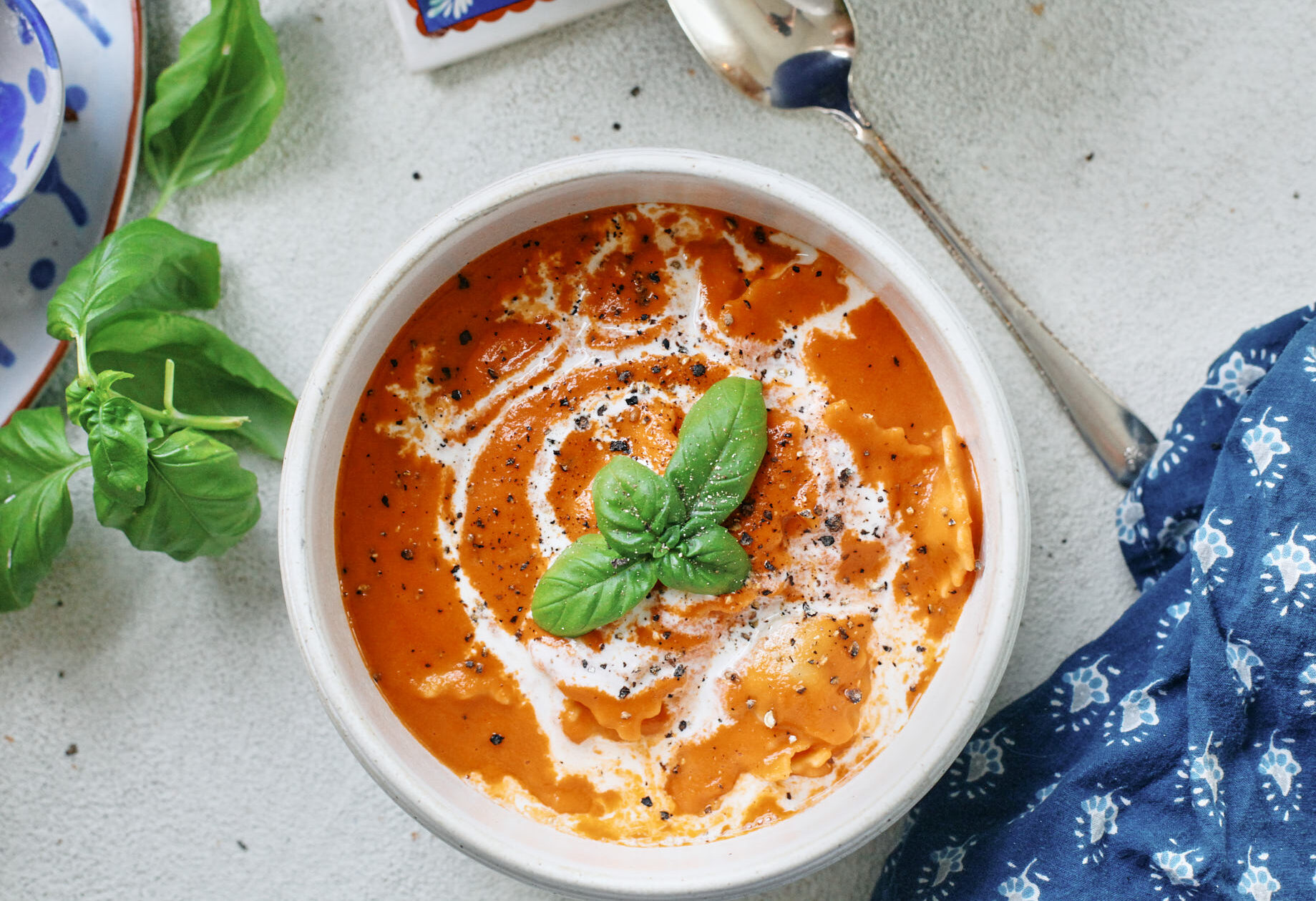 Creamy Tomato Ravioli Soup in a white bowl with basil garnish and a drizzle of cream, perfect cozy dinner recipe