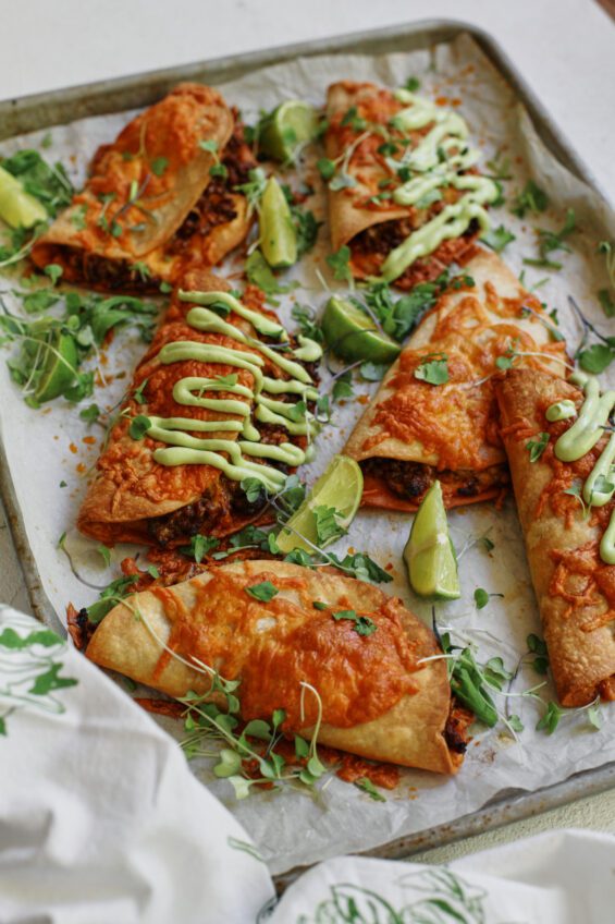 sheet pan beef tacos dressed with avocado lime crema, cilantro, and lime wedges
