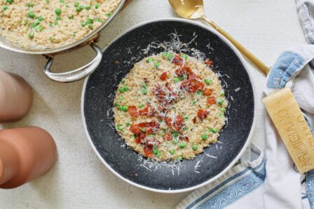 cheesy bacon pastina with peas, served in a black bowl