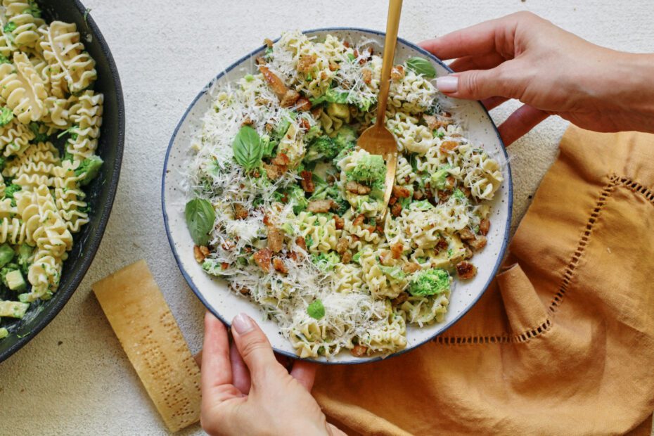 two hands placing a bowl of broccoli caesar pasta salad down on the table