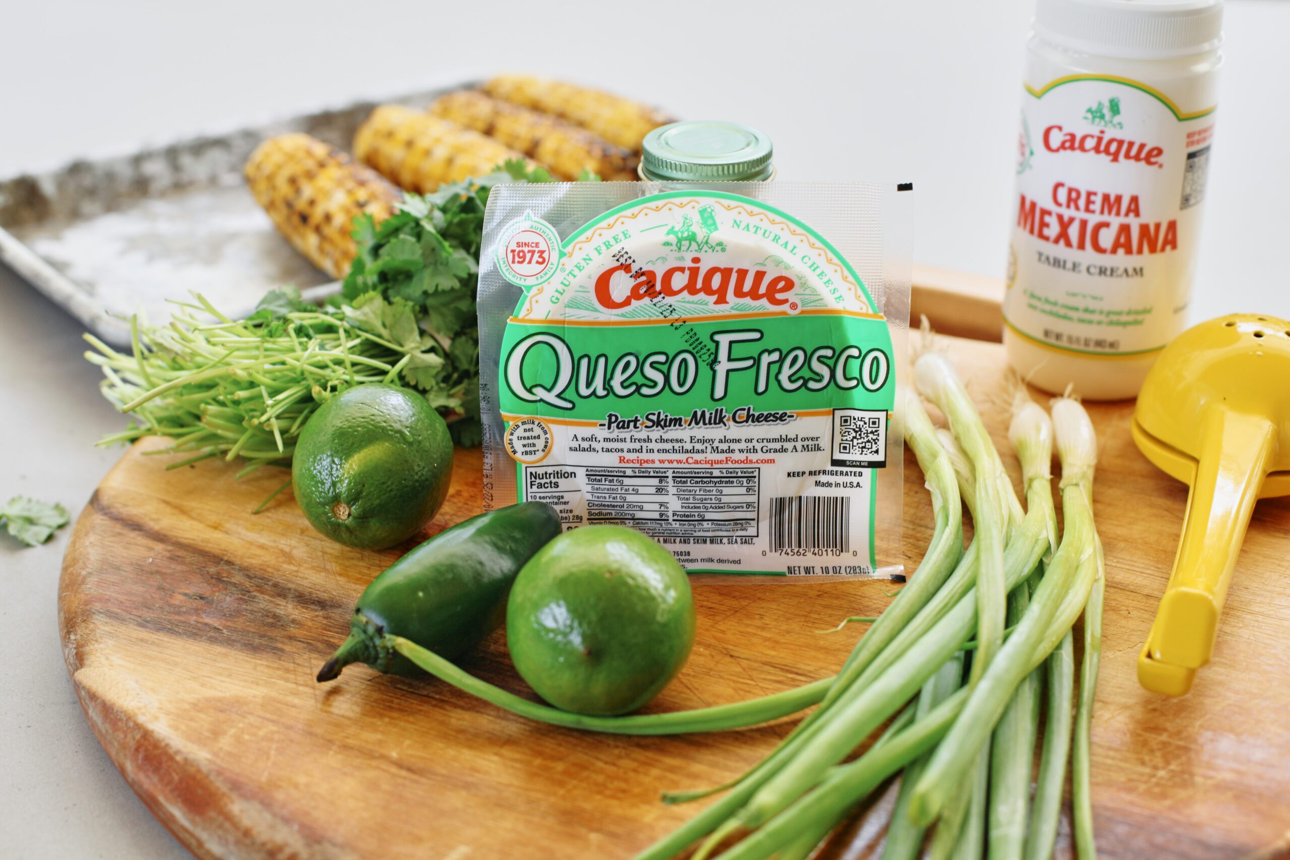 Ingredients prepped for elote pasta salad: queso fresco, crema mexicana, roasted corn, green onions, jalapeno, cilantro, limes