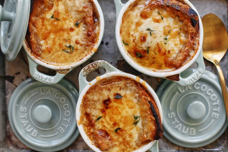 french onion soup in mini green dutch ovens that are arranged on a sheet pan, topped with golden, melted cheese