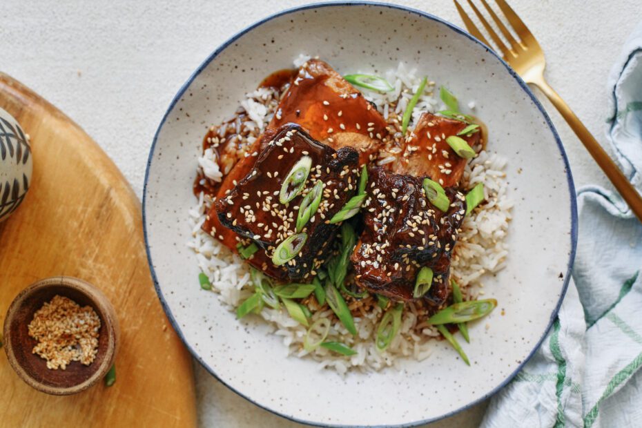 sticky soy and citrus short ribs over white rice, garnished with green onions and sesame seeds