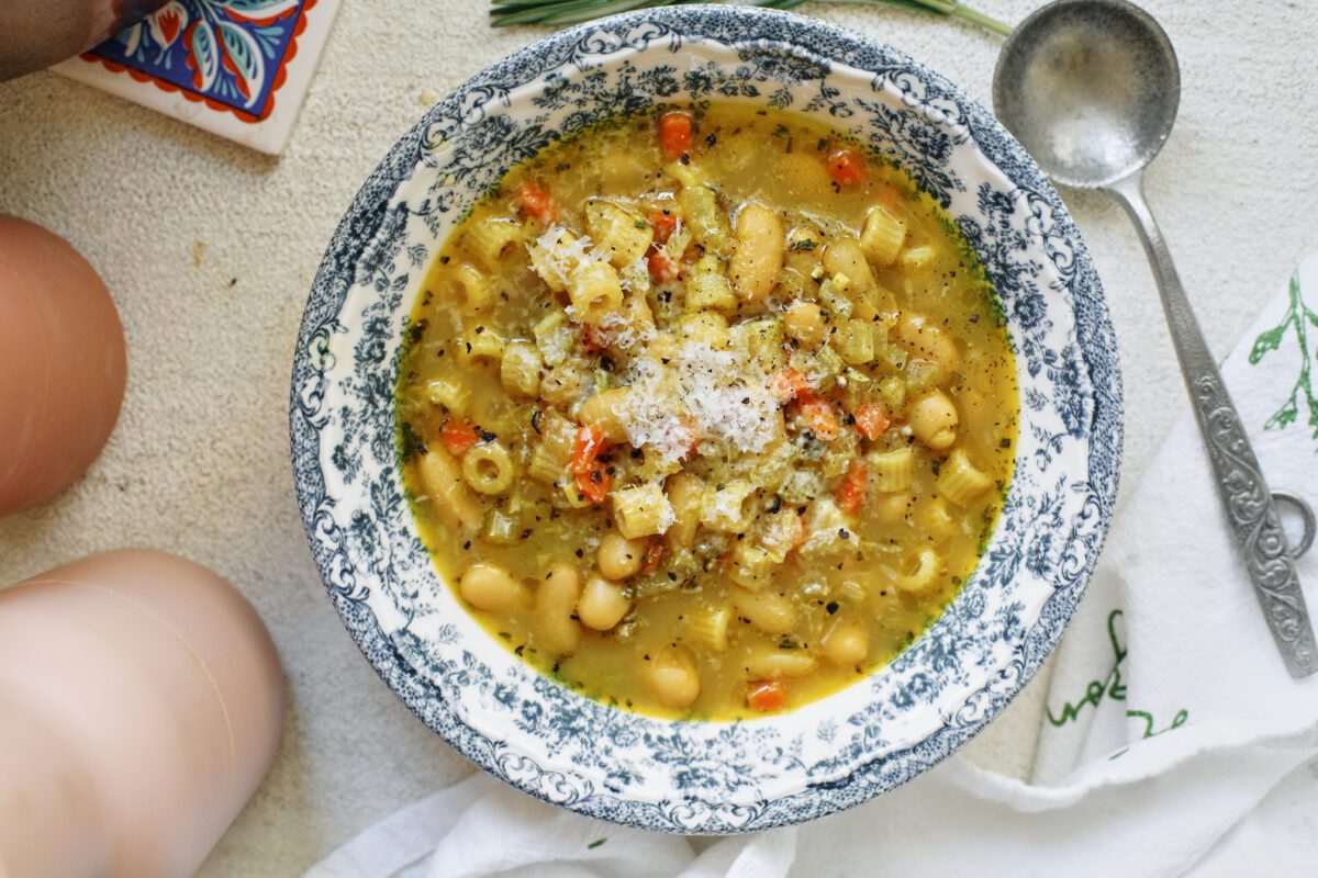 overhead photo of pasta e fagioli alla bianca in a blue/white floral patterned bowl. it's garnished with grated parmesan cheese and black pepper. an antique-looking silver spoon is next to the bowl