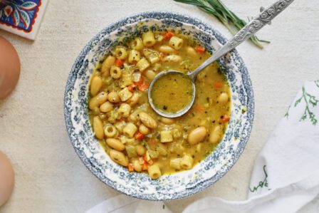 overhead photo of pasta e fagioli alla bianca in a blue/white floral patterned bowl. an antique-looking silver spoon is in the bowl