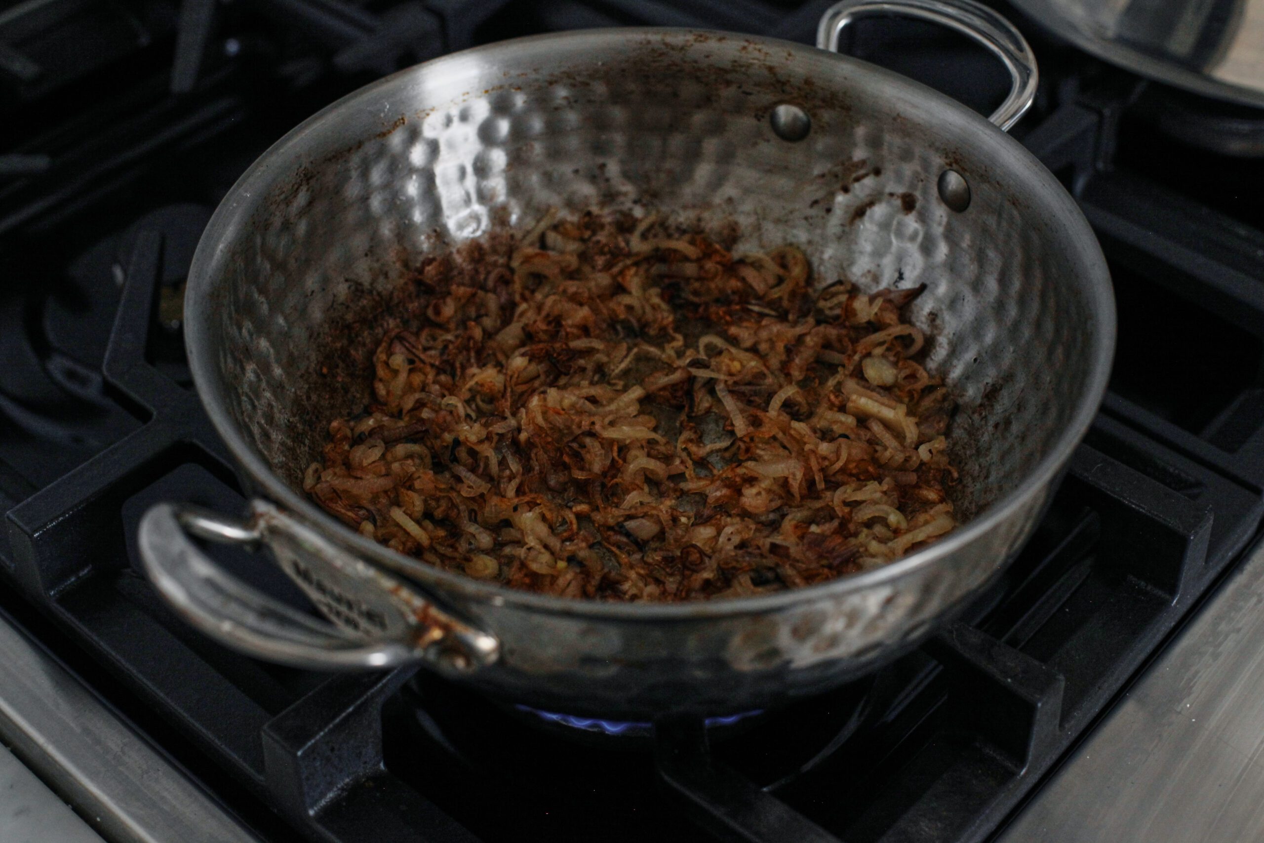 shallots caramelizing in a hammered steel sauté pan on a gas range