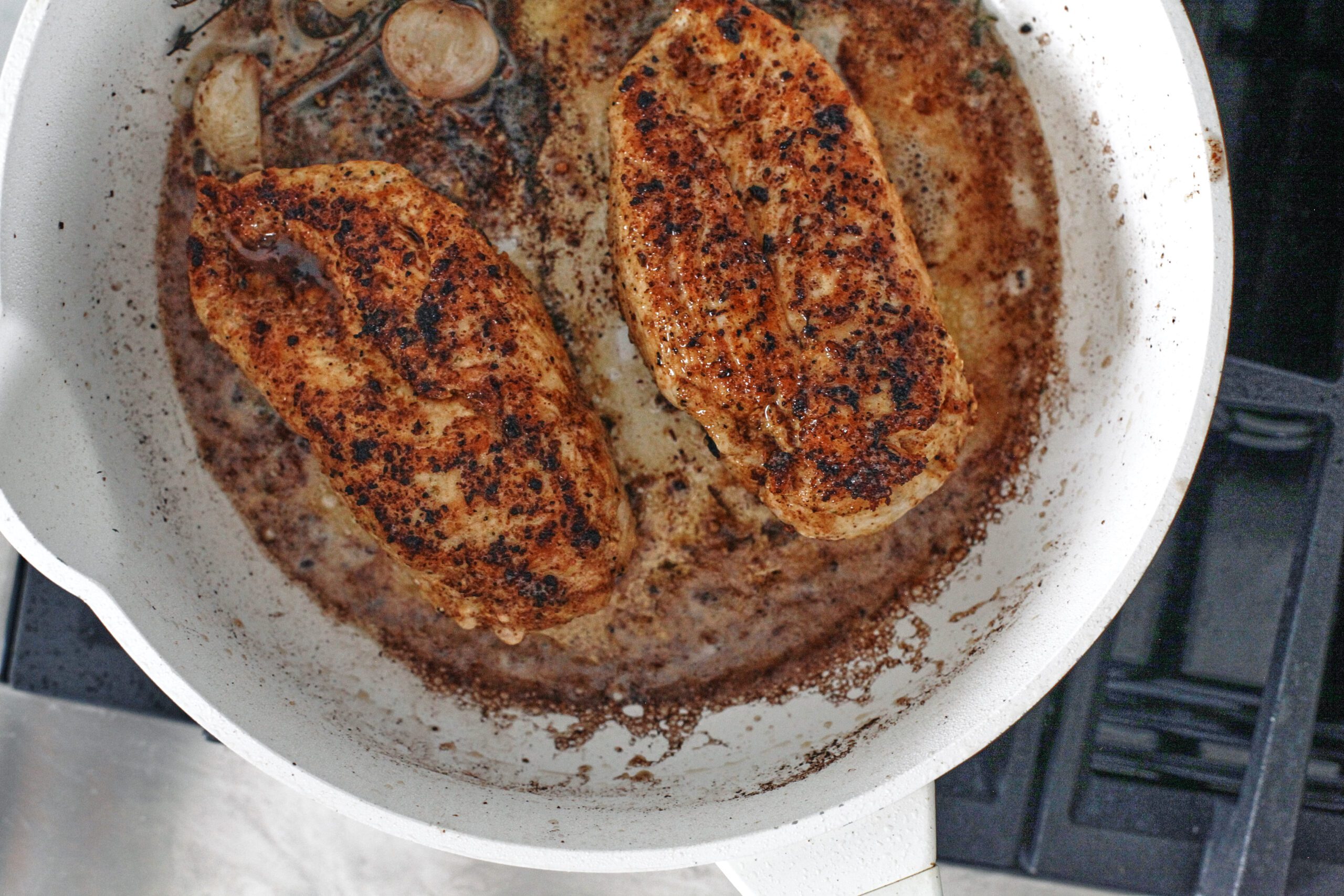 2 chicken breasts being seared in a large white pan