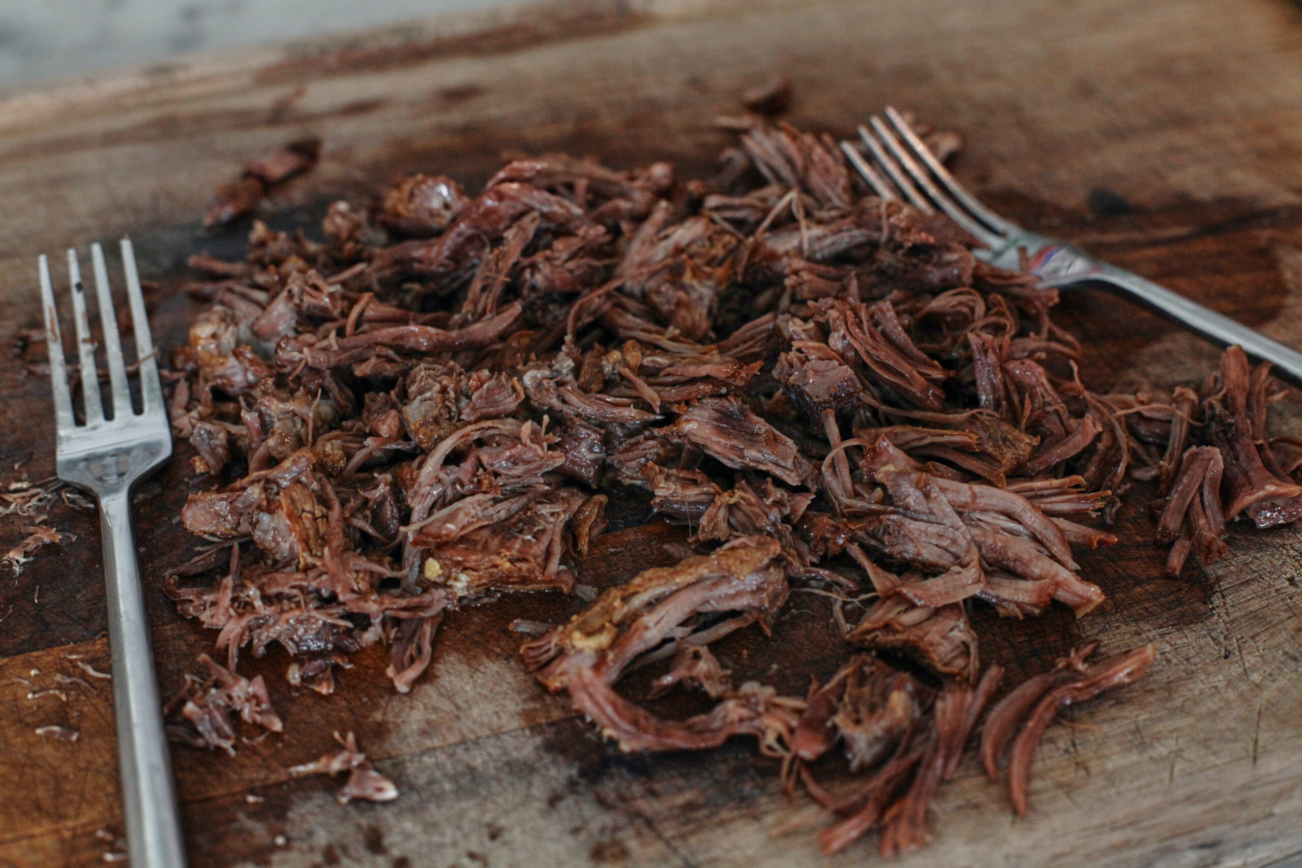 a pile of beef short rib meat shredded off the bone on a wood cutting board with two forks