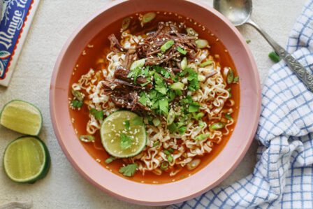 beef short rib noodle soup in a light pink bowl, garnished with half a lime, sesame seeds, and cilantro