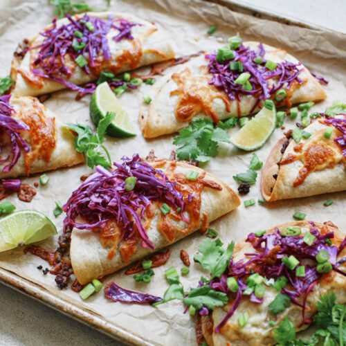 korean style beef sheet pan tacos with purple cabbage slaw, sriracha aioli, cilantro, green onions, sesame seeds, and lime wedges