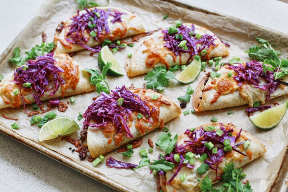 korean style beef sheet pan tacos with purple cabbage slaw, sriracha aioli, cilantro, green onions, sesame seeds, and lime wedges