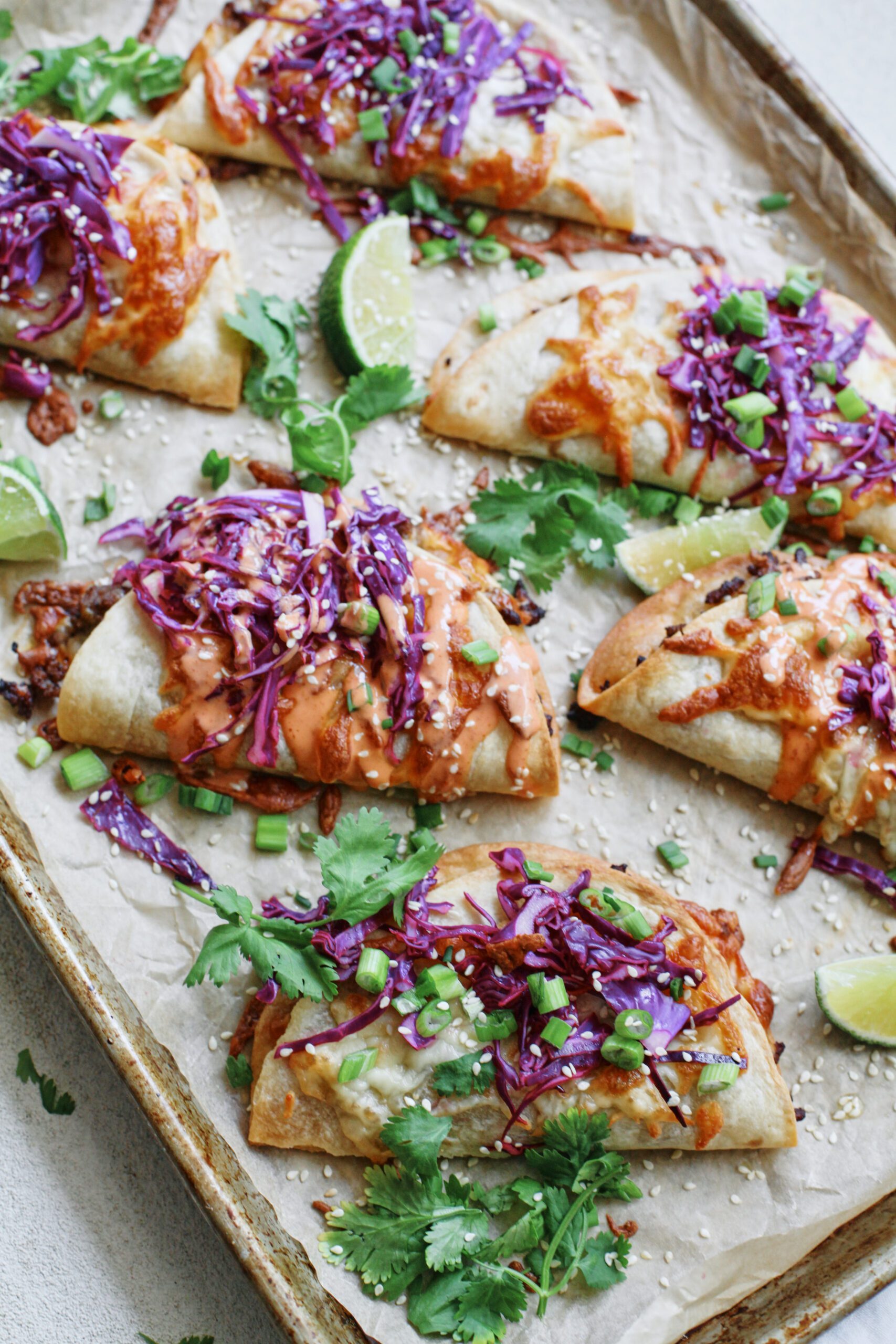 korean style beef sheet pan tacos with purple cabbage slaw, sriracha aioli, cilantro, green onions, sesame seeds, and lime wedges
