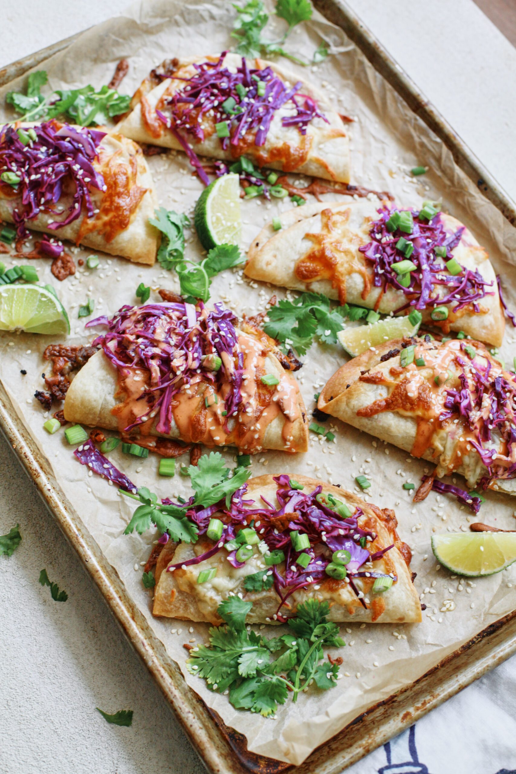 korean style beef sheet pan tacos with purple cabbage slaw, sriracha aioli, cilantro, green onions, sesame seeds, and lime wedges