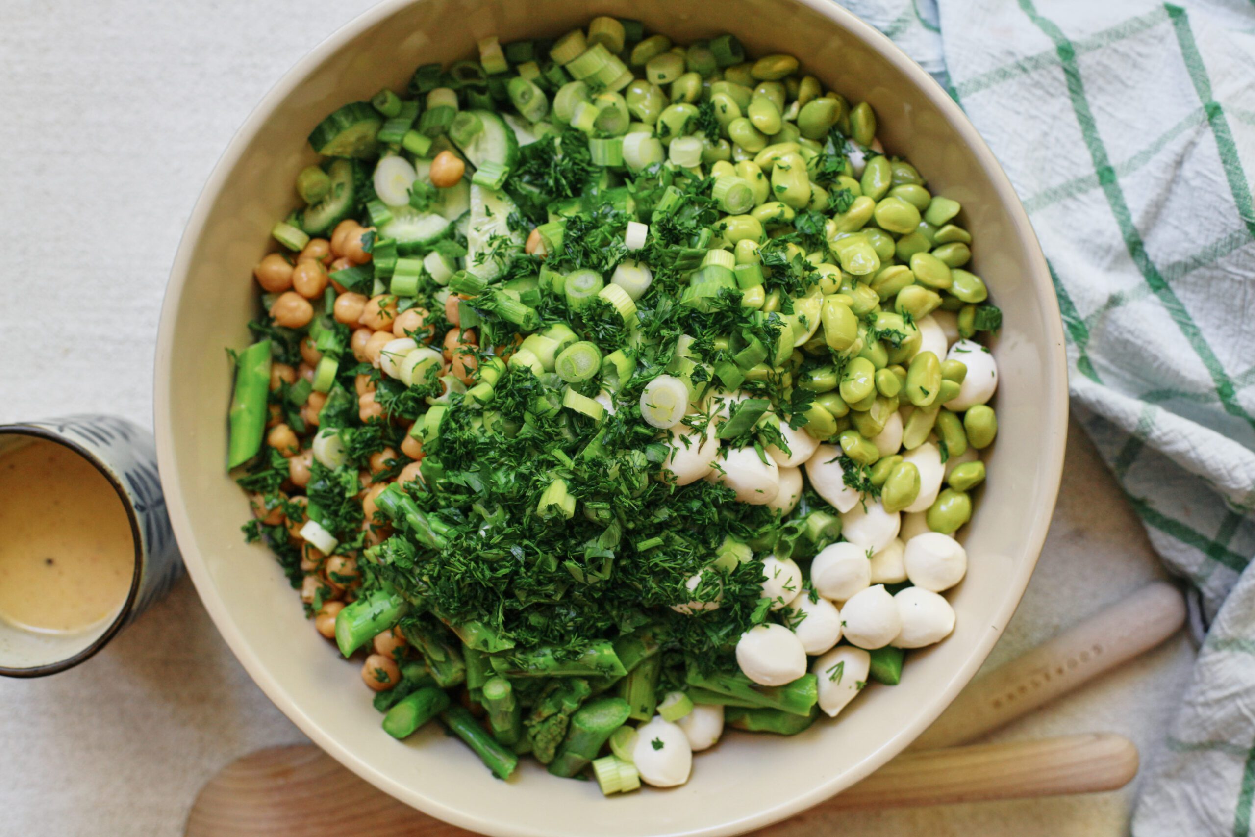 pasta salad before being mixed: chickpeas, cucumbers, green onions, mozzarella pearls, parsley, edamame, and asparagus poured into a large bowl with cooked orecchiette