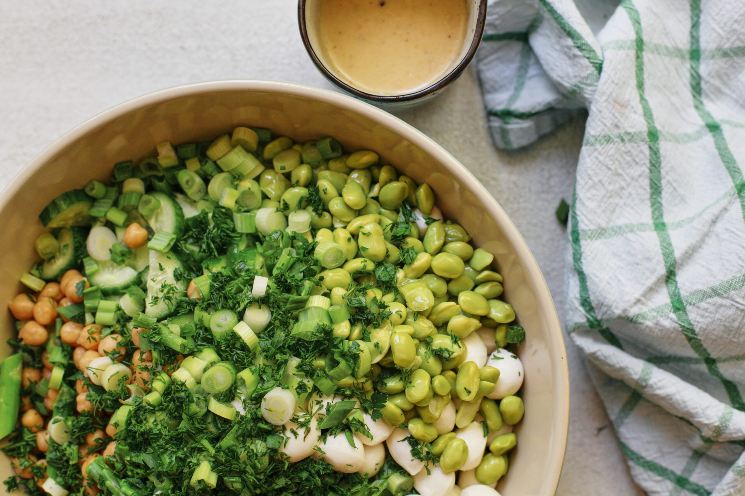 pasta salad before being mixed: chickpeas, cucumbers, green onions, mozzarella pearls, parsley, edamame, and asparagus poured into a large bowl with cooked orecchiette