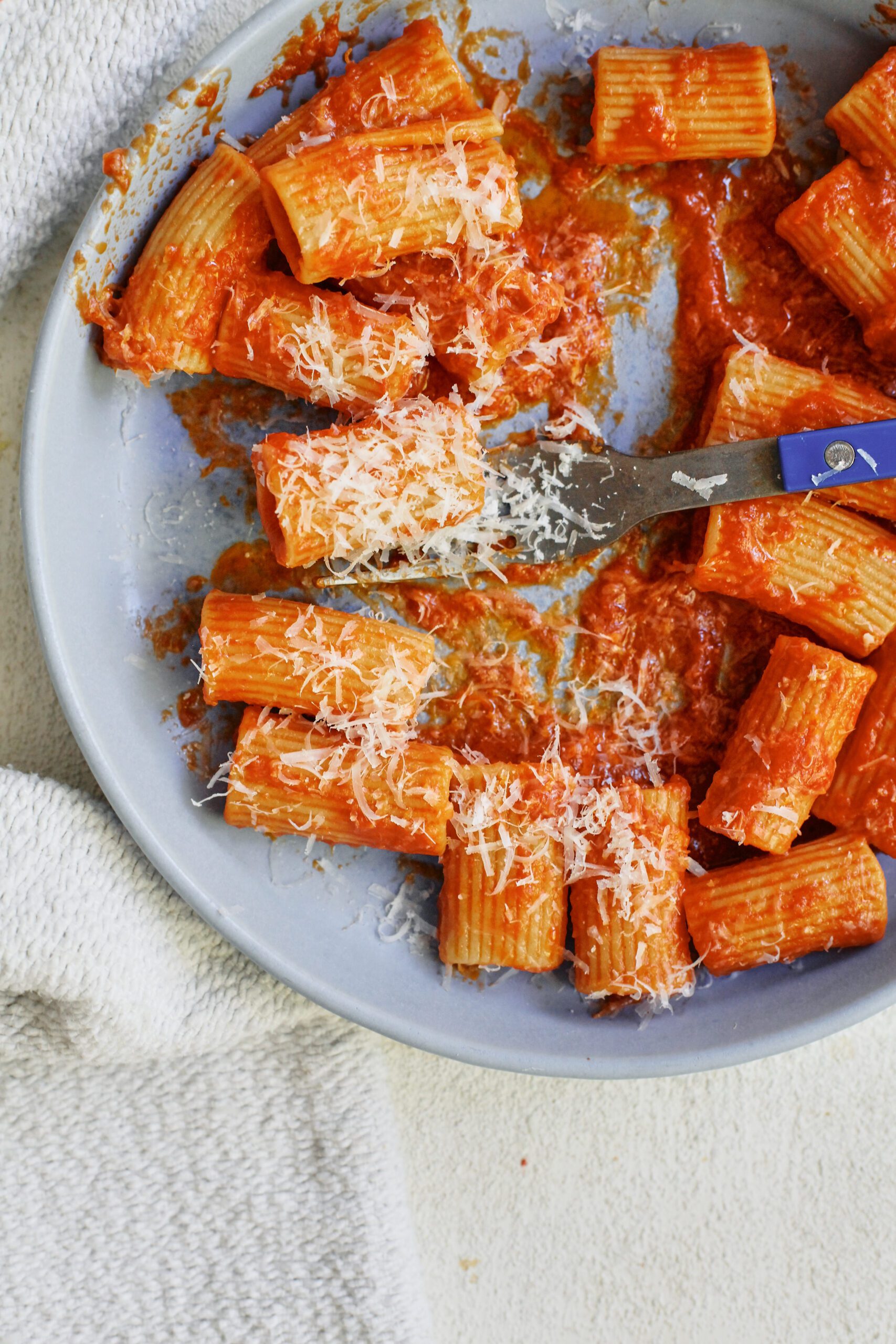 Tomato ginger butter rigatoni on a light blue plate with a blue-handled fork