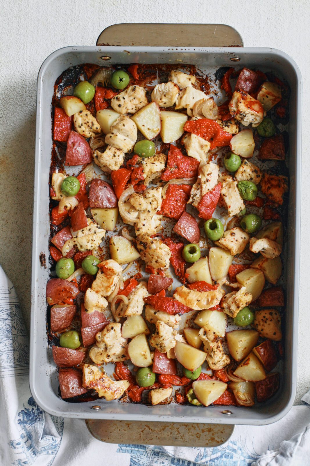 ingredients in a baking dish after being roasted in the oven: cubed chicken breast, chopped baby red potatoes, sliced shallot, green olives, chopped roasted red peppers