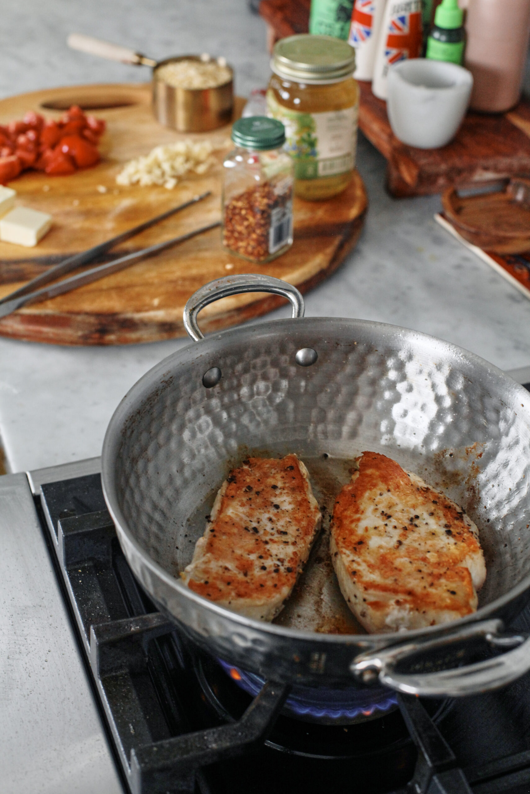two chicken breasts searing in a hammered steel saute pan