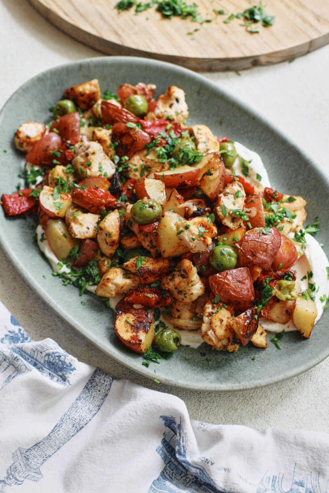 Mediterranean Chicken & Potato Tray Bake (cubed chicken breast, chopped baby red potatoes, sliced shallot, green olives, and chopped roasted red peppers) served over a yogurt sauce on an oval teal-coloured platter