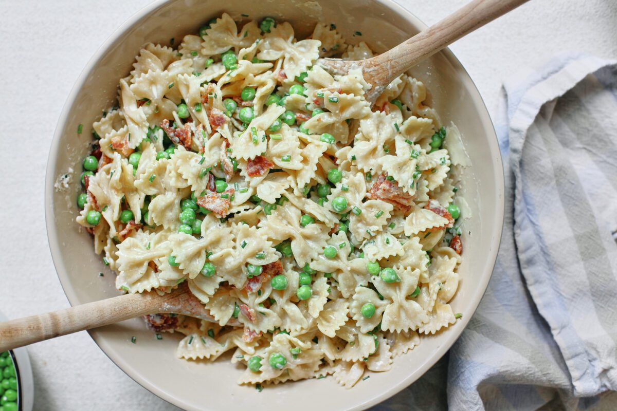 bacon, peas, and parmesan pasta salad in a large bowl with two wooden serving spoons