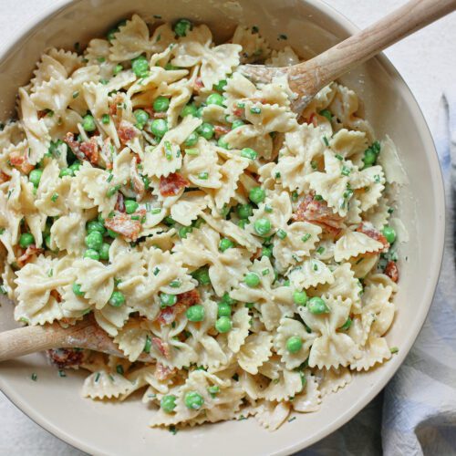 bacon, peas, and parmesan pasta salad in a large bowl with two wooden serving spoons