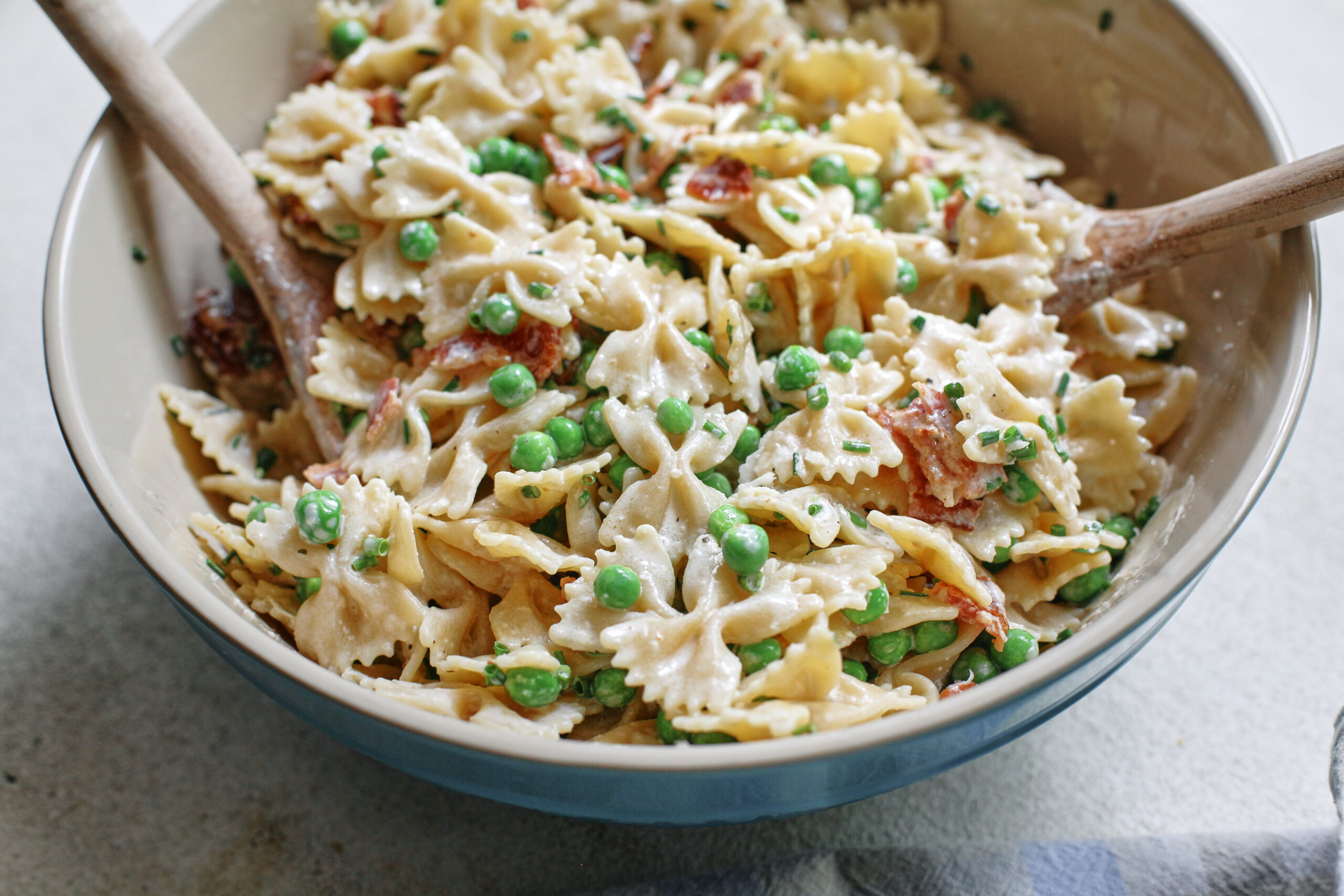 bacon, peas, and parmesan pasta salad in a large bowl with two wooden serving spoons