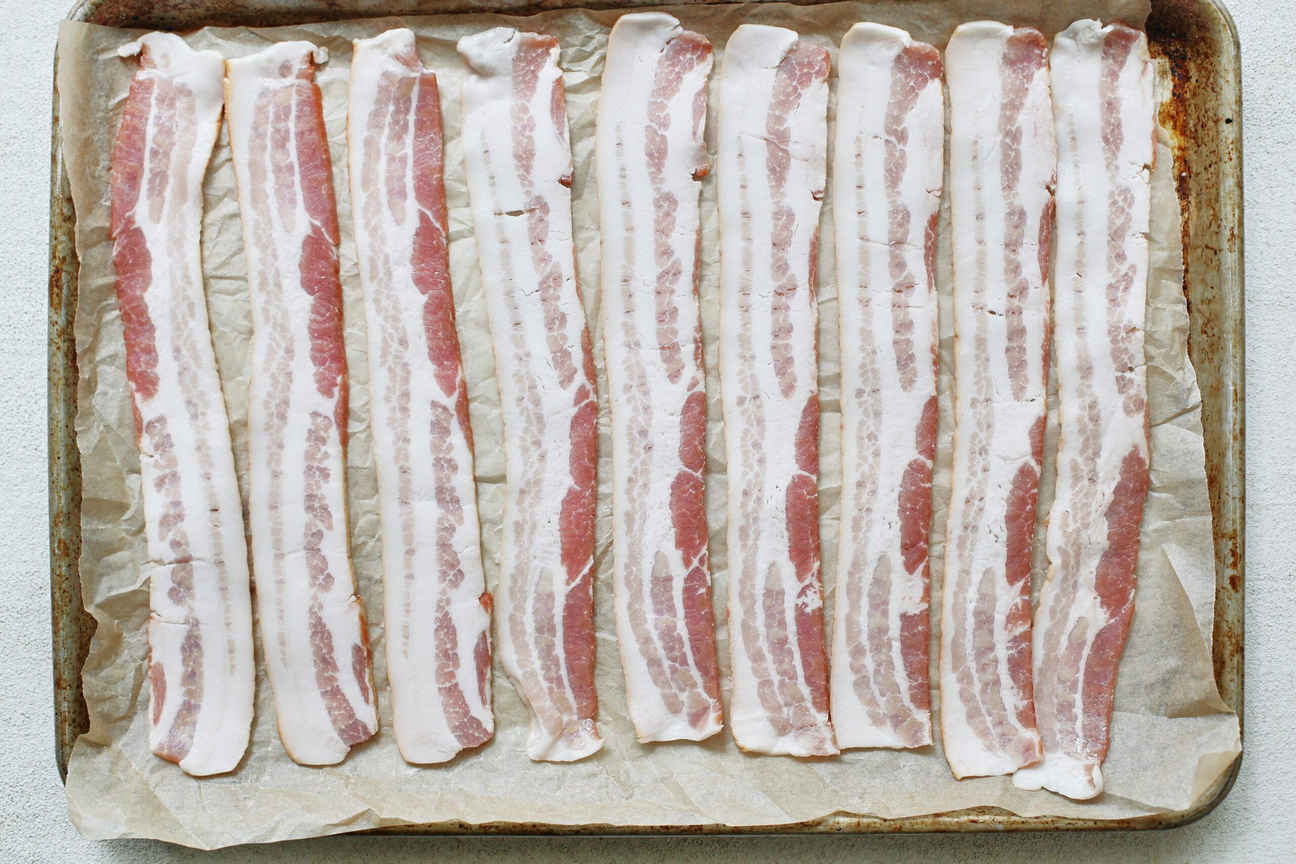 9 strips of raw bacon on a parchment paper-lined baking sheet