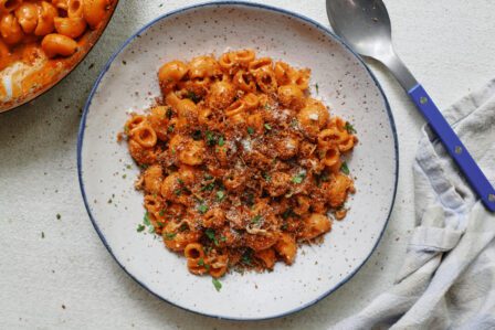 creamy vodka pasta topped with toasted garlic breadcrumbs, in a speckled white bowl with a blue-handled spoon to the side of the bowl