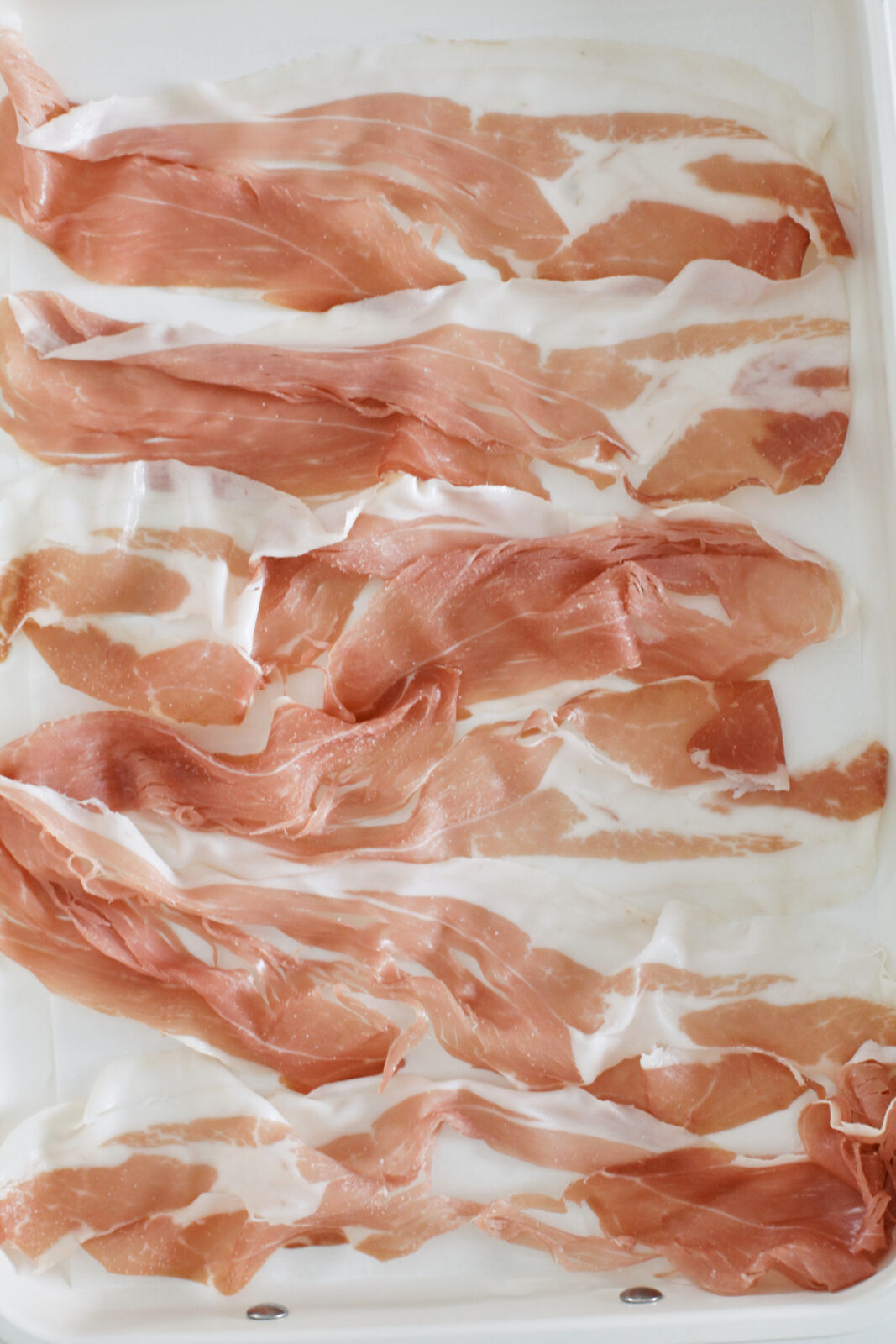 six slices of prosciutto laid out on a parchment-line baking sheet