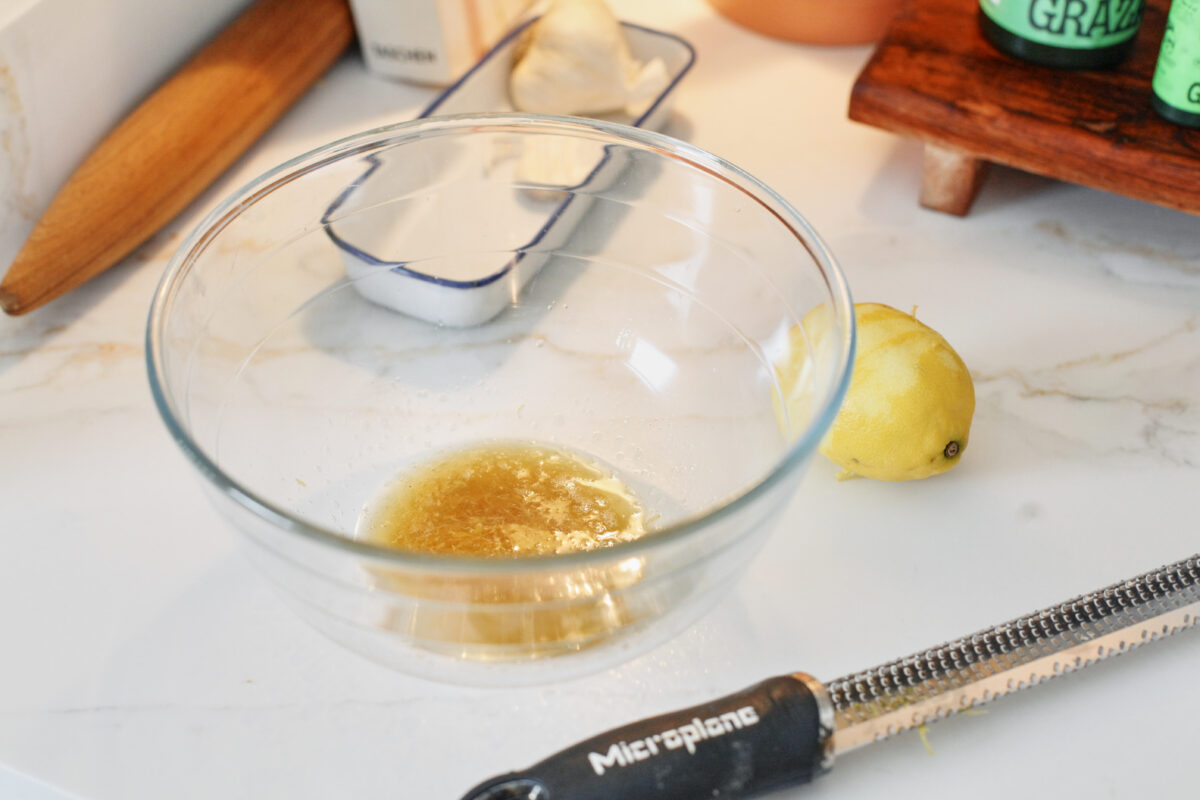 browned butter with lemon zest mixed into it in a large glass bowl, and a lemon to the right side of the bowl