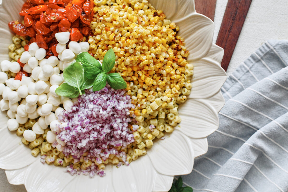 Roasted corn pesto pasta salad ingredients arranged in a white flower-shaped serving bowl