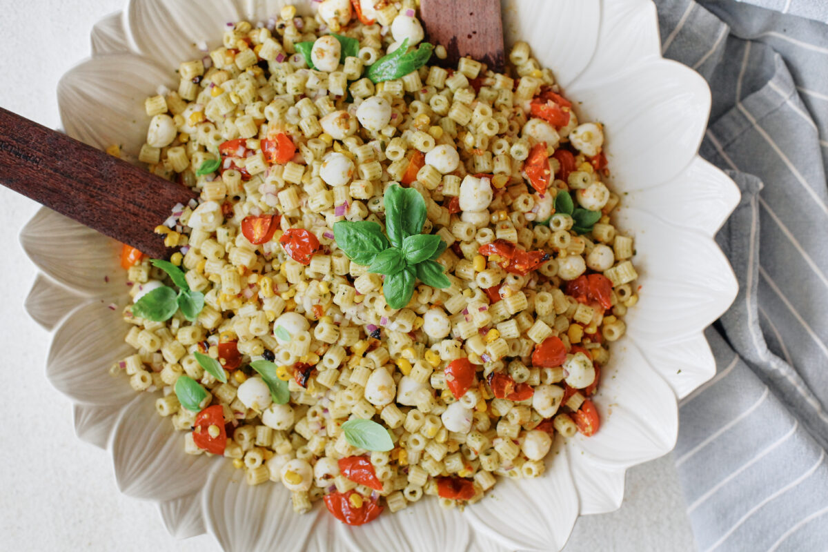 Overhead view of roasted corn pesto pasta salad served in a white flower-shaped bowl