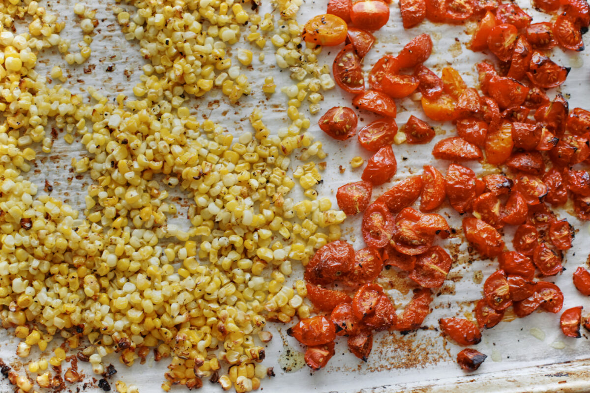 Close-up of roasted corn and cherry tomatoes with caramelized edges on a sheet pan