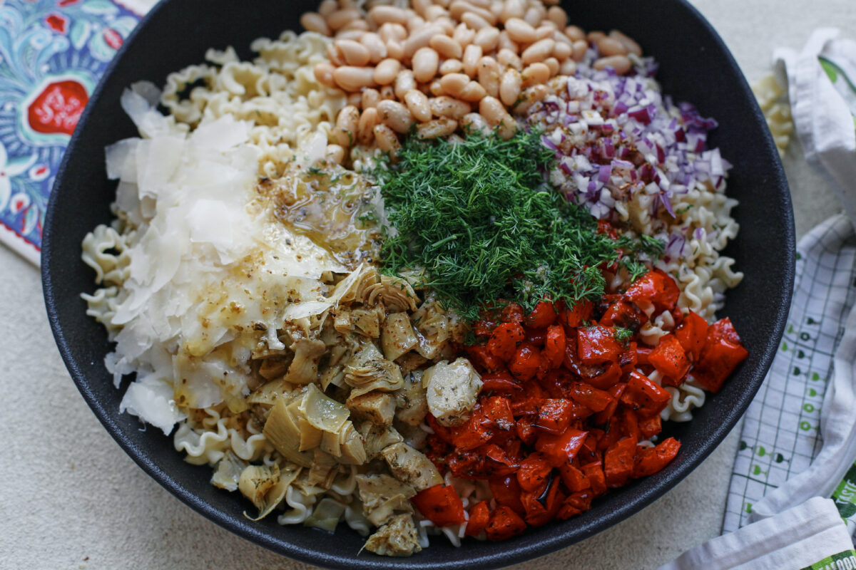 Overhead view of antipasto pasta salad ingredients in a large serving bowl, drizzled with vinaigrette and ready to be tossed together