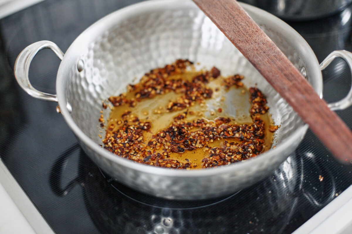 chili oil heating in a hammered steel saute pan on the stove