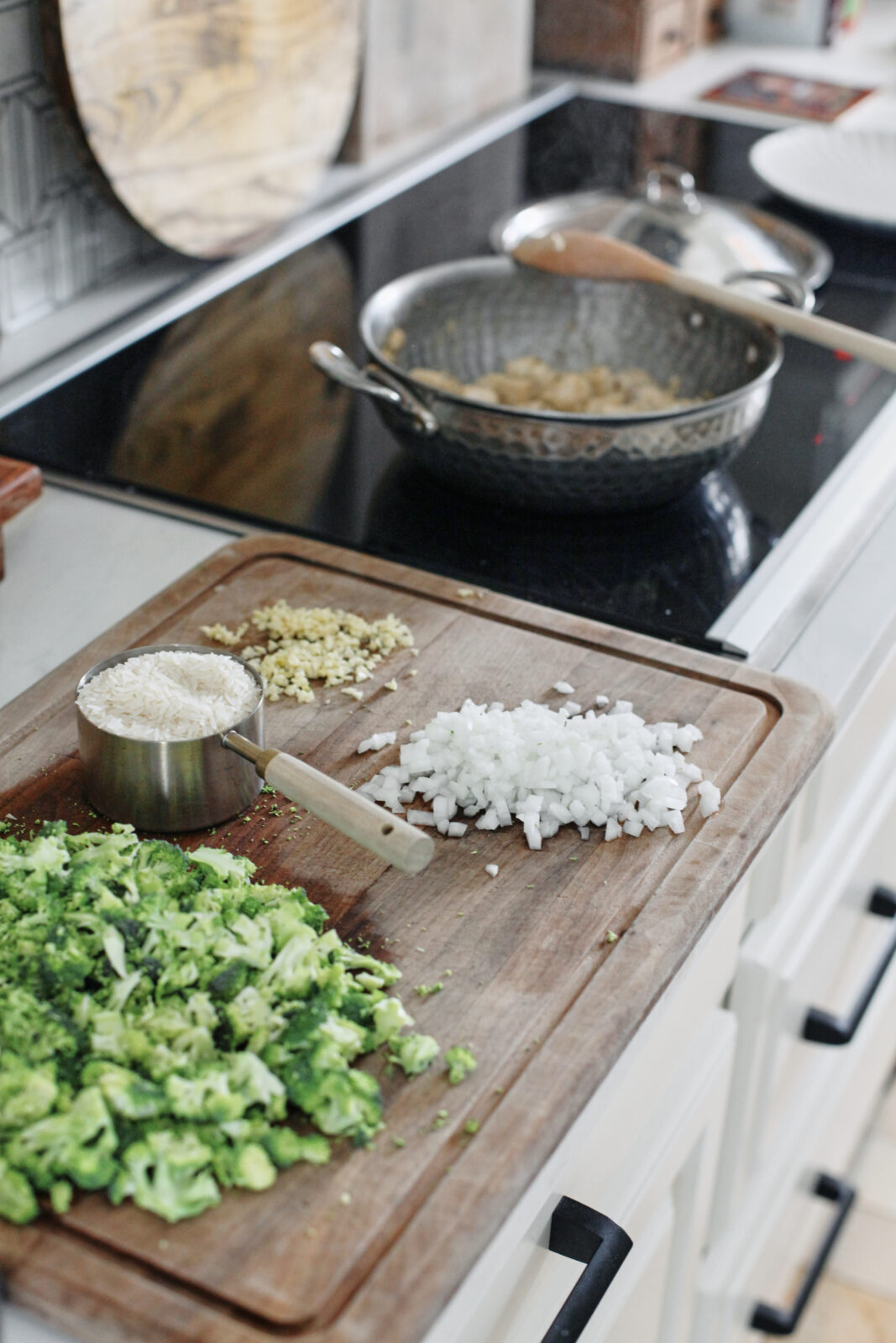 cutting board with chopped broccoli, a cup of rice, chopped onion, and minced garlic