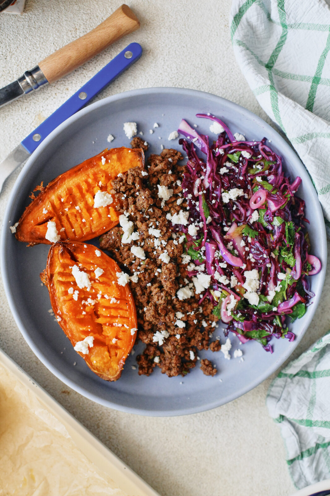 Ground beef taco sweet potato bowls topped with purple cabbage cilantro lime slaw and crumbled queso fresco in a shallow ceramic bowl