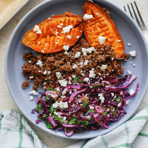 Ground beef taco sweet potato bowls topped with purple cabbage cilantro lime slaw and crumbled queso fresco in a shallow ceramic bowl