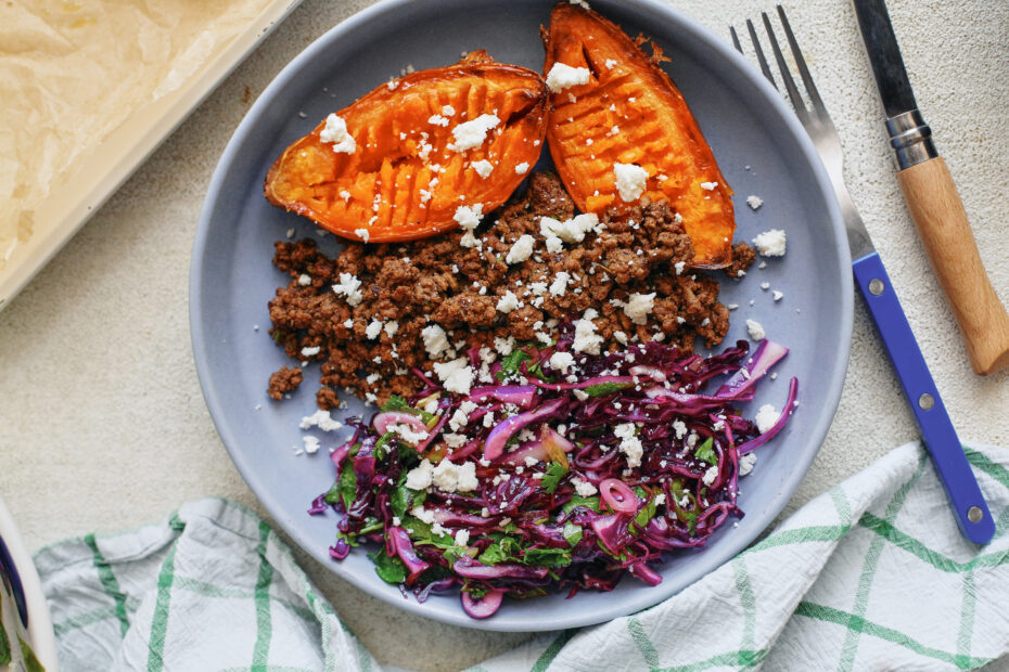 Ground beef taco sweet potato bowls topped with purple cabbage cilantro lime slaw and crumbled queso fresco in a shallow ceramic bowl