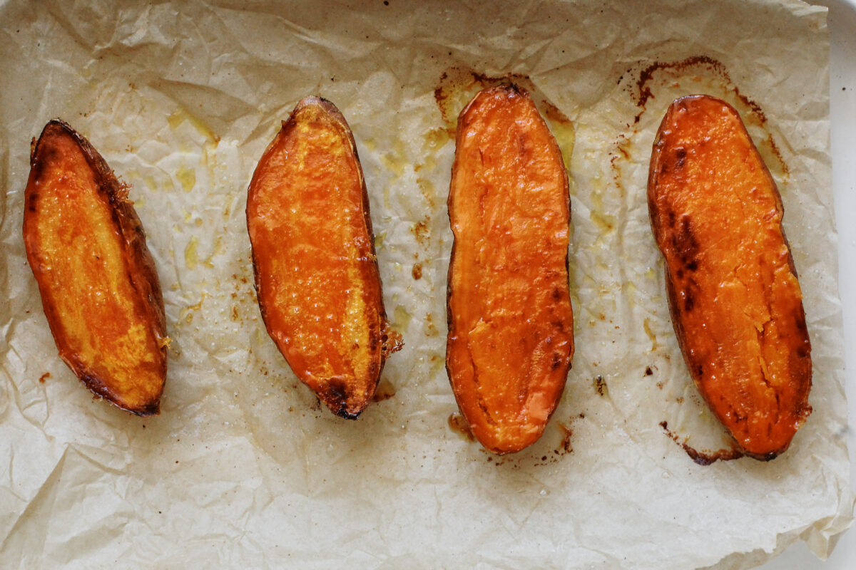 Roasted sweet potato halves cut-side down on a parchment-lined sheet pan with caramelized edges