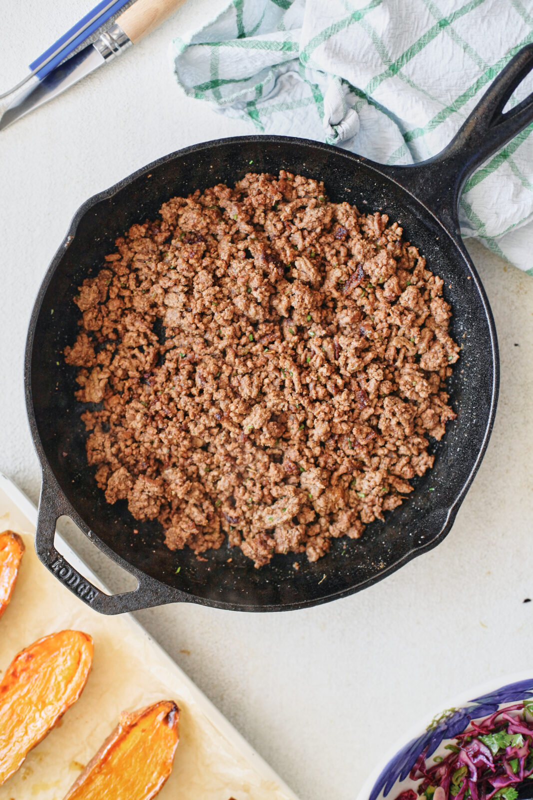 Seasoned ground beef browning in a skillet with cumin, chili powder, and chopped cilantro stems