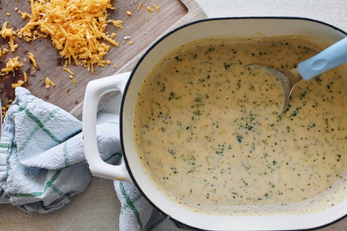 a large white dutch oven with the broccoli cheddar soup and a small blue ladle in it