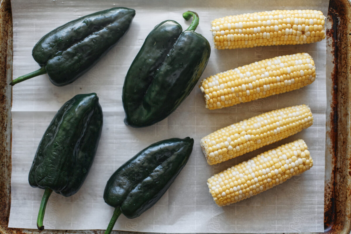 four poblano peppers and four ears of corn on a parchment-lined baking sheet