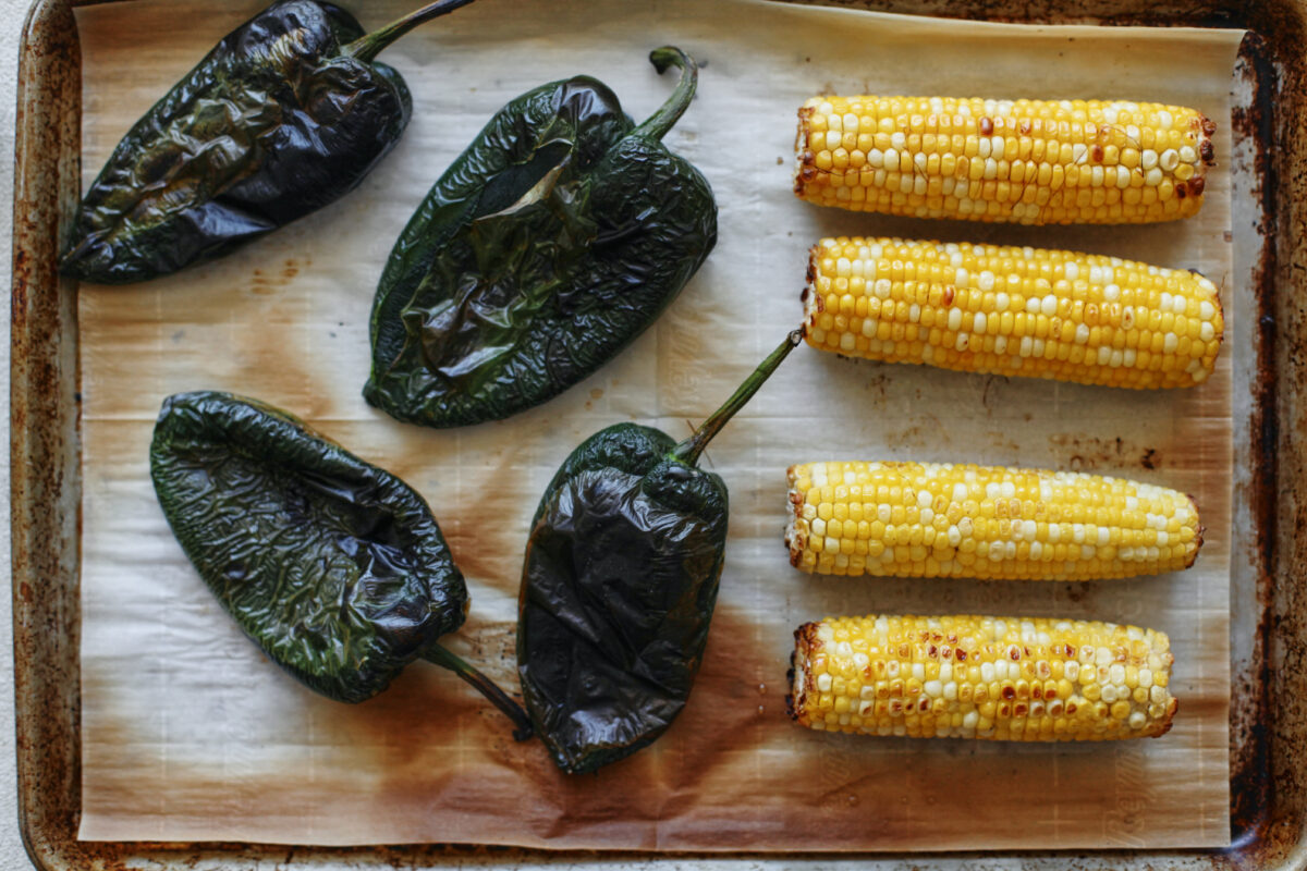 four poblano peppers and four ears of corn on a parchment-lined baking sheet after being broiled